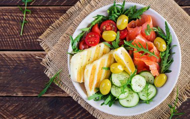 Ketogenik, keto diyeti. Tuzlu somon, ızgara halloumi peyniri, kiraz domatesleri ve beyaz kasede zeytinli salatalık. Sağlıklı yiyecekler. Üst görünüm, yukarıda