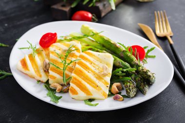Izgara halloumi peynirli salata, domatesli ve koyu arkaplanda kuşkonmaz. Sağlıklı vejetaryen yemekleri.