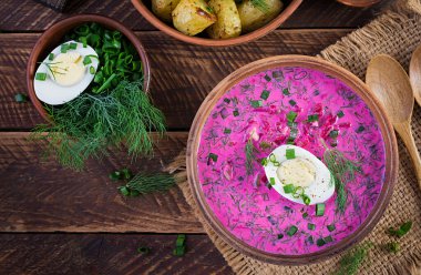 Soğuk borş, taze salatalıklı pancar çorbası, haşlanmış yumurta ve ahşap masada fırında patates. Geleneksel Avrupa yemekleri, lezzetli öğle yemekleri. Üst görünüm, genel görünüm
