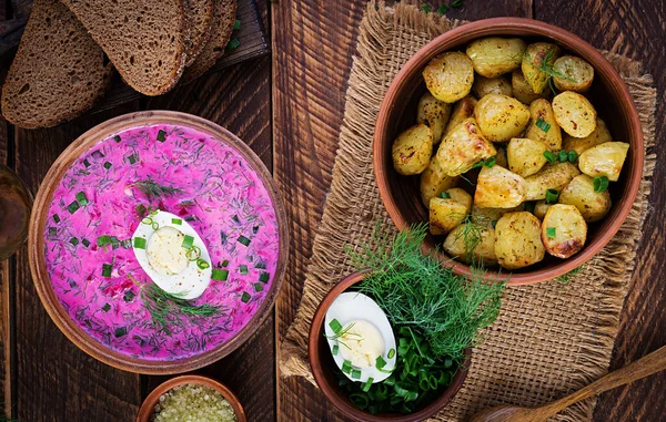 冷罗宋汤 夏季甜菜汤 新鲜黄瓜 煮熟的鸡蛋和烤土豆放在木制桌子上 传统的欧洲食物 美味的午餐 顶视图 — 图库照片