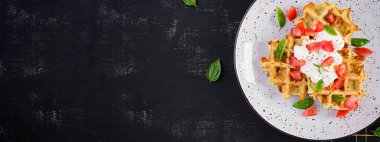 Kabaklı waffle, waffle makinesinde pişen kabaklı börek, domatesli vejetaryen kabaklı waffle, beyaz tabakta ekşi krema ve fesleğen. Üst görünüm, afiş