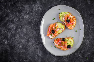 Krem peynirli tost, füme somon, salatalık, siyah zeytin ve kırmızı soğan. Sandviç aç. Sağlıklı bakım, süper gıda konsepti. Üst görünüm, genel görünüm