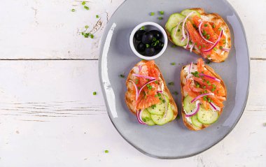 Krem peynirli tost, füme somon, salatalık ve ahşap masada kırmızı soğan. Sandviç aç. Sağlıklı bakım, süper gıda konsepti. Üst görünüm, genel görünüm