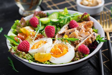 Izgara tavuk eti ve taze sebze salatası. Domates, salatalık, yumurta, marul ve ahududu. Ketogenik diyet. Buda çanağı koyu arkaplanda.