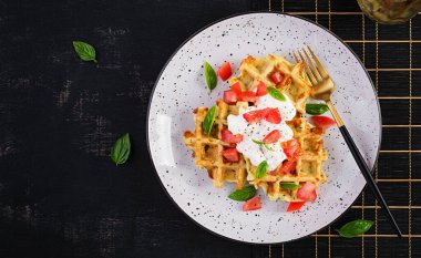 Kabaklı waffle, waffle makinesinde pişen kabaklı börek, domatesli vejetaryen kabaklı waffle, beyaz tabakta ekşi krema ve fesleğen. Üst manzara, düz uzanma