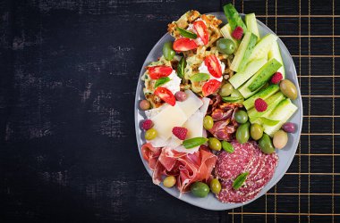 Şarküteri tahtası. Prosciutto, salam, salam, salatalık ve zeytinli parmesan. Lezzetli aperatifler ya da antipastalar. Üst görünüm, kopyalama alanı, düz uzanma