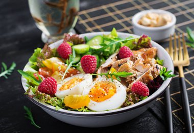 Izgara tavuk eti ve taze sebze salatası. Domates, salatalık, yumurta, marul ve ahududu. Ketogenik diyet. Buda çanağı koyu arkaplanda.