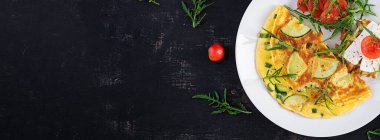 Kabaklı omlet, yeşil otlar ve tabakta peynirli sandviç. Frittata - İtalyan omleti. Üst görünüm, yukarıda, afiş