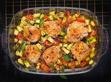 Fırınlanmış tavuk butları, kabak ve sebzeler karanlık bir masada pişirme kabında. Üst görünüm, genel görünüm