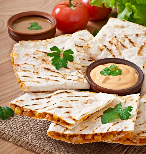 Mexican Quesadilla sliced with vegetables and sauces on the table