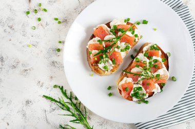 İki açık sandviç, somonlu tost, krem peynir, beyaz tabakta sağlıklı kahvaltı için yeşil soğan. Üst görünüm