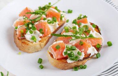 Two open sandwich, toast with salmon, cream cheese, green onions for healthy breakfast on white plate.