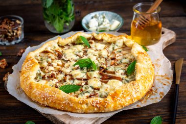 Ahşap masada fırında galet ya da açık turta, armut, mavi peynir ve fındık..