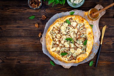 Ahşap masada fırında galet ya da açık turta, armut, mavi peynir ve fındık. Üst görünüm