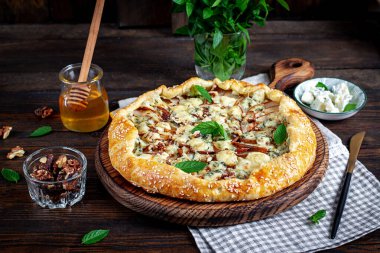 Ahşap masada fırında galet ya da açık turta, armut, mavi peynir ve fındık..