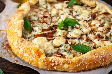 Ahşap masada fırında galet ya da açık turta, armut, mavi peynir ve fındık..