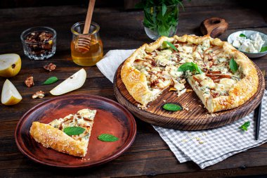 Ahşap masada fırında galet ya da açık turta, armut, mavi peynir ve fındık..