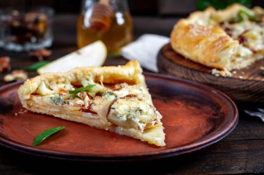 Ahşap masada fırında galet ya da açık turta, armut, mavi peynir ve fındık..
