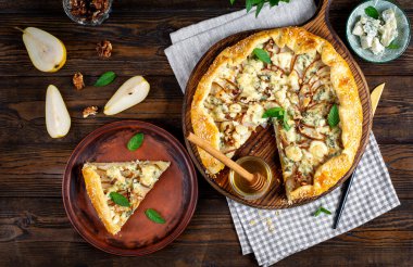 Ahşap masada fırında galet ya da açık turta, armut, mavi peynir ve fındık. Üst görünüm