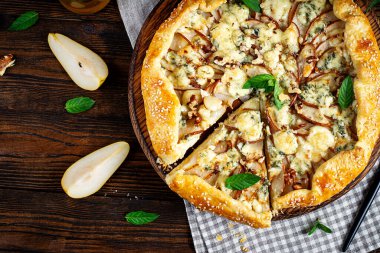 Ahşap masada fırında galet ya da açık turta, armut, mavi peynir ve fındık. Üst görünüm