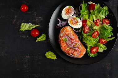 Lezzetli sağlıklı kahvaltı - haşlanmış yumurta, somon balığı ve yeşil salata. Koyu arkaplanda dengeli yemek tabağı, üst görünüm, kopyalama alanı.