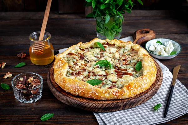 Ahşap masada fırında galet ya da açık turta, armut, mavi peynir ve fındık..