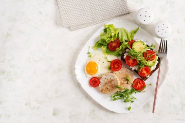 İngiliz kahvaltısı. Yağda yumurta, tavuklu köfte ve domatesli sandviç, avokado ve peynir. Üst görünüm