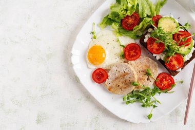 İngiliz kahvaltısı. Yağda yumurta, tavuklu köfte ve domatesli sandviç, avokado ve peynir. Üst görünüm