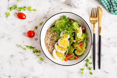 Sağlıklı kahvaltı kasesi yulaf ezmesi, haşlanmış yumurta ve taze sebze. Üst görünüm