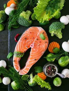 Çiğ somon steak ve karanlık bir arka plan bir rustik tarzda yemek pişirmek için malzemeler. Üstten Görünüm