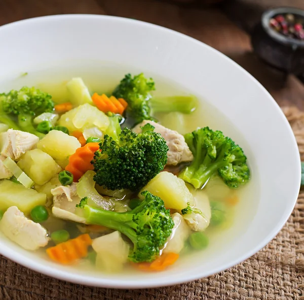 Kippensoep met broccoli, groene erwten, wortelen en BLEEKSELDERIJ in een witte kom op een houten achtergrond — Stockfoto