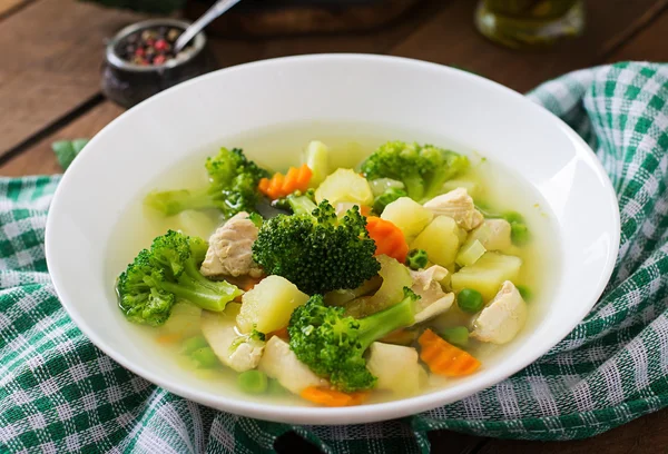 Kippensoep met broccoli, groene erwten, wortelen en BLEEKSELDERIJ in een witte kom op een houten achtergrond — Stockfoto