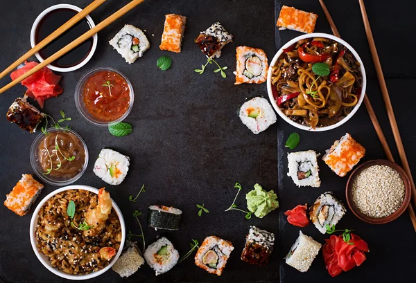 Traditionelles japanisches Essen - Sushi, Semmeln, Reis mit Garnelen und Udonnudeln mit Huhn und Pilzen auf dunklem Hintergrund. — Stockfoto