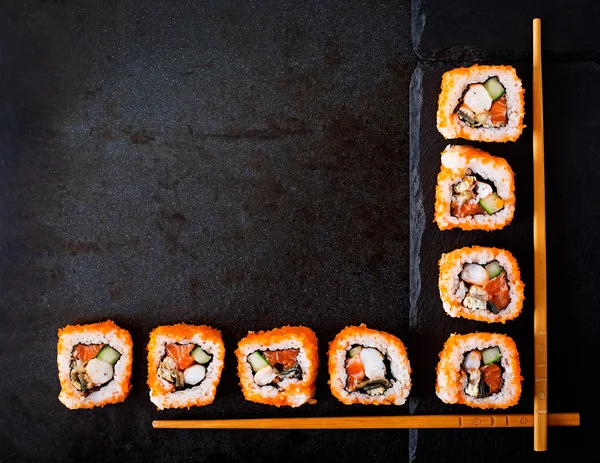 Tradiční japonské jídlo - sushi, rohlíky a hůlky pro sushi na tmavém pozadí. — Stock fotografie