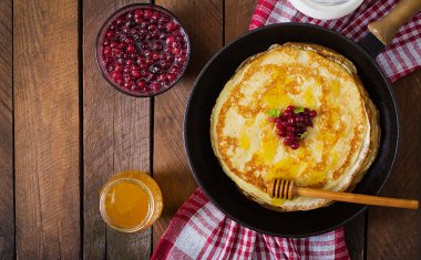 Golden pancakes with cranberry jam and honey in a rustic style