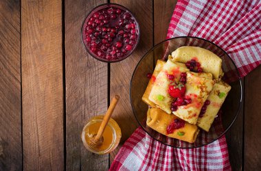 Golden pancakes with cranberry jam and honey in a rustic style.