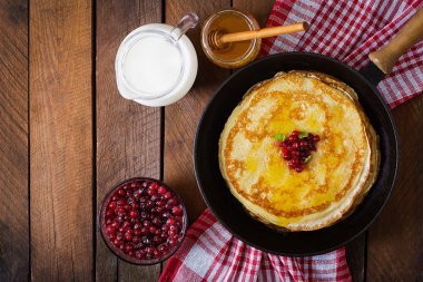 Golden pancakes with cranberry jam and honey in a rustic style