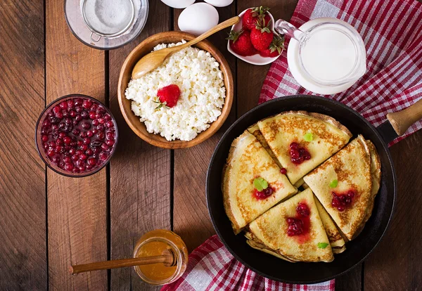 Golden pancakes with cranberry jam and honey in a rustic style