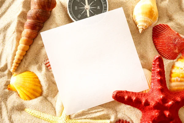 Seashells, compass and paper on sand — Stock Photo, Image