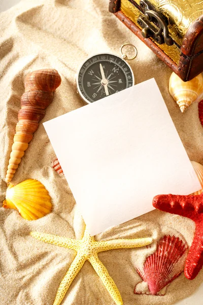 Ракушки, компас и бумага на песке — стоковое фото