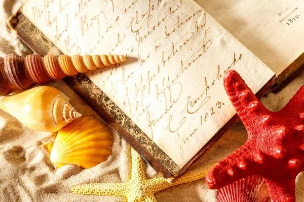 Seashells and old book on sand — Stock Photo, Image