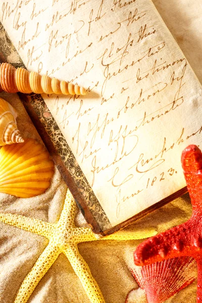 Seashells and old book on sand — Stock Photo, Image