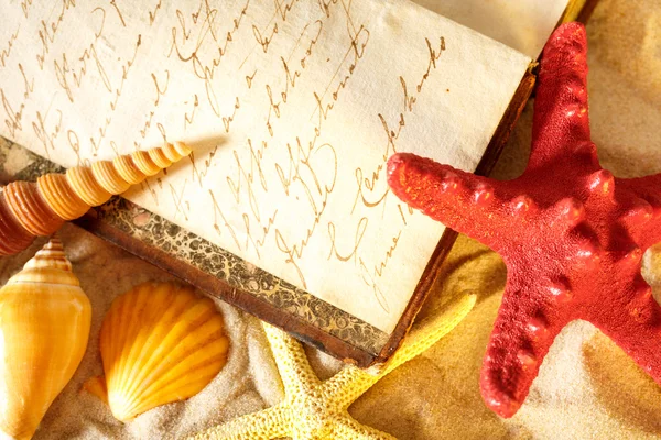 Seashells and old book on sand — Stock Photo, Image