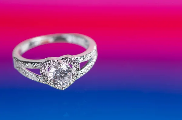 Heart-shaped ring with a crystal on a red-blue background.