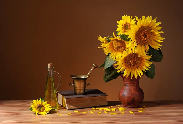 Zonnebloemen in een vaas, boeken en olie in een fles — Stockfoto