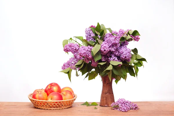 Las lilas moradas en un jarrón y una manzana —  Fotos de Stock