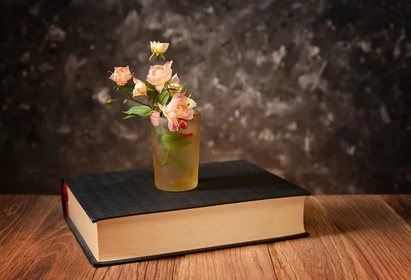 Fiori in un bicchiere e un libro — Foto Stock