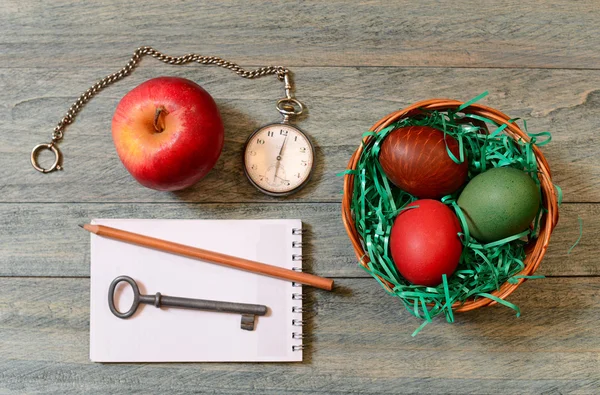 Uova di Pasqua in un cesto, mela e orologio da tasca — Foto Stock