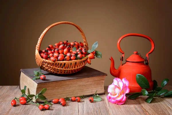 Rosehip in wicker baskets, book, rose and a teapot — Stock Photo, Image