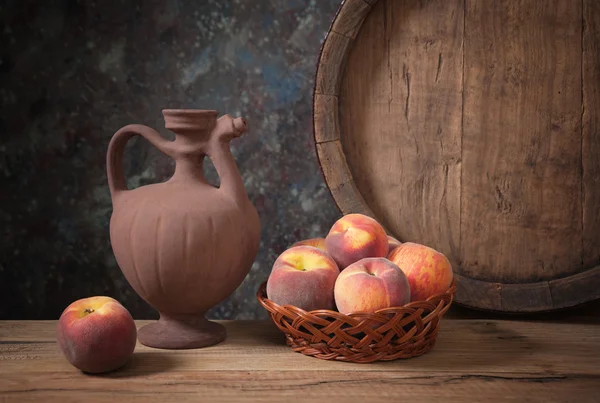 Fresh peaches in a wicker basket and her pitcher — Stock fotografie